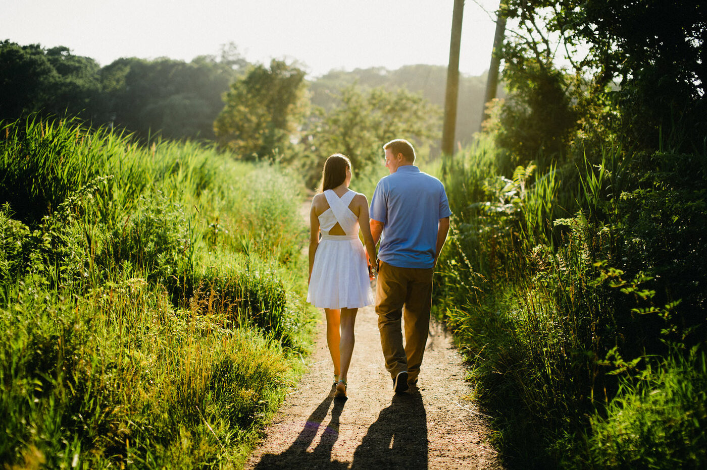 A couple walking hand in hand down a sunlit path